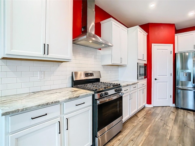 kitchen with backsplash, stainless steel appliances, wall chimney exhaust hood, white cabinets, and light hardwood / wood-style floors