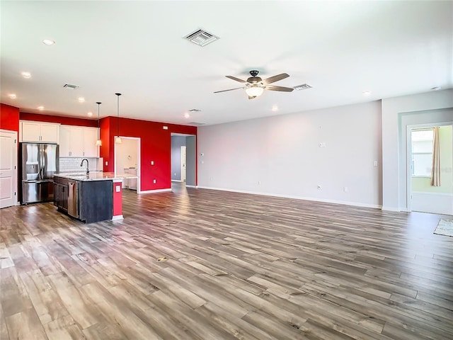 unfurnished living room featuring visible vents, ceiling fan, baseboards, and wood finished floors