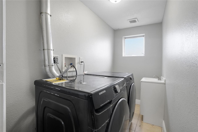 clothes washing area featuring washing machine and dryer, light tile patterned floors, and sink