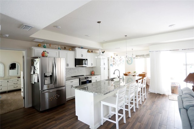 kitchen with a breakfast bar area, a center island with sink, appliances with stainless steel finishes, dark wood-type flooring, and sink