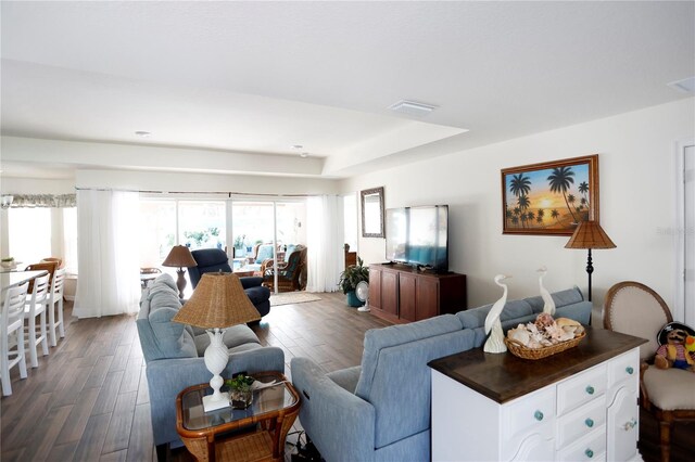 living room featuring a raised ceiling and dark hardwood / wood-style flooring