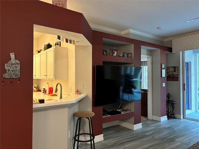 kitchen featuring hardwood / wood-style flooring, white cabinetry, sink, a kitchen breakfast bar, and ornamental molding