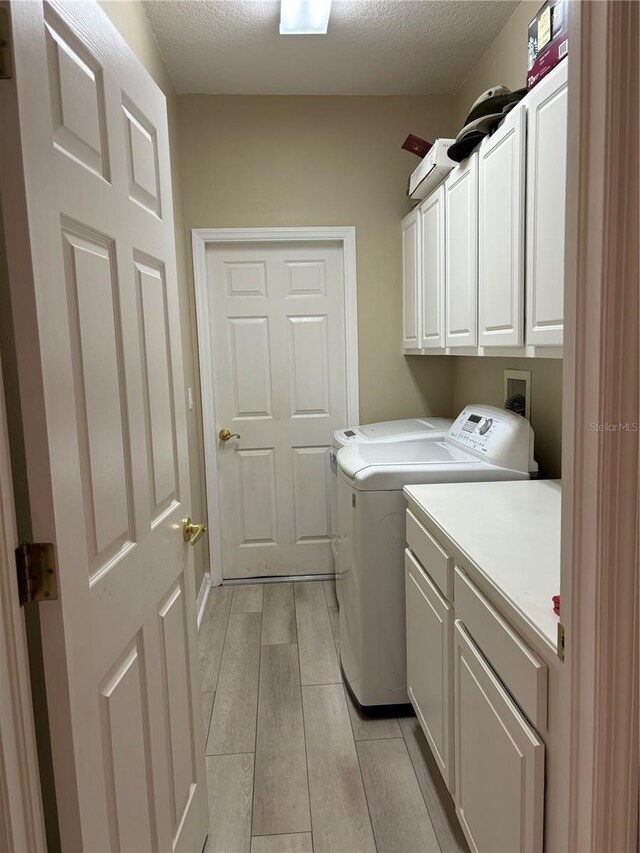 clothes washing area with washer and clothes dryer, a textured ceiling, cabinets, and light hardwood / wood-style flooring