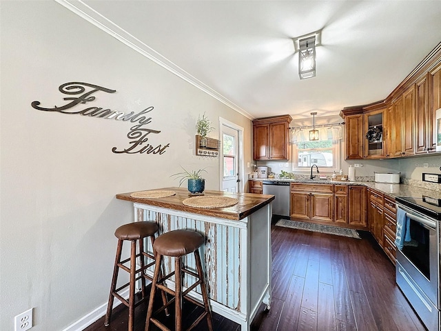 kitchen with dark hardwood / wood-style floors, appliances with stainless steel finishes, crown molding, hanging light fixtures, and a breakfast bar