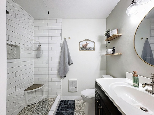 bathroom featuring tile patterned flooring, vanity, toilet, and a tile shower