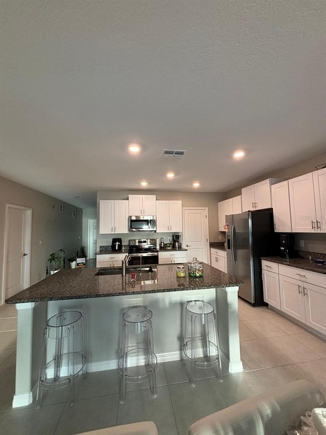 kitchen featuring appliances with stainless steel finishes, a center island with sink, white cabinetry, and a breakfast bar