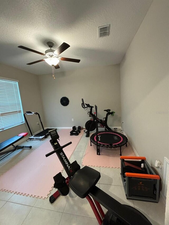 exercise area with a textured ceiling, ceiling fan, and tile patterned flooring