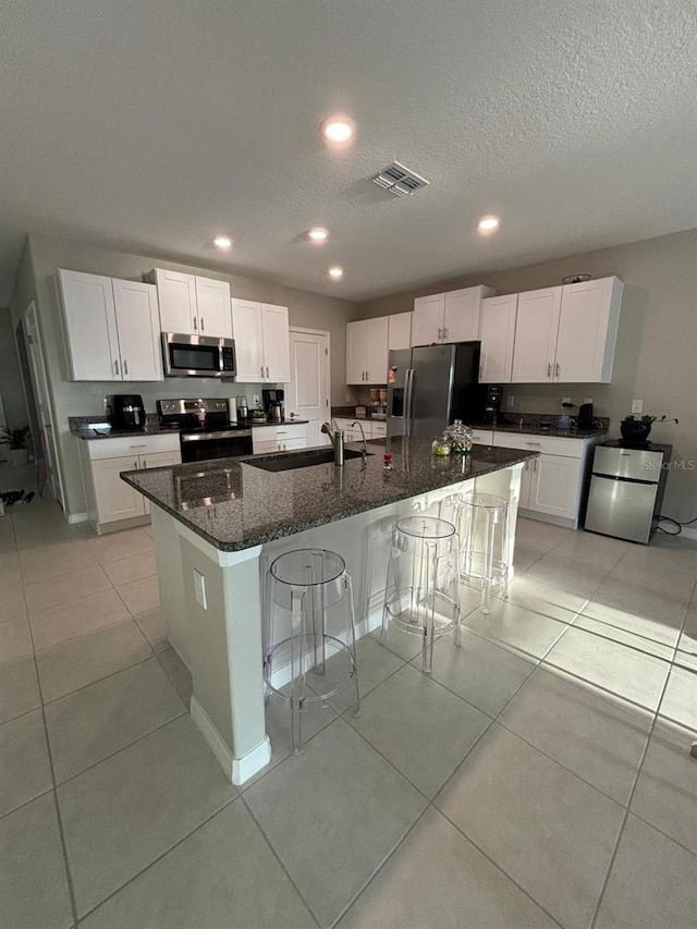 kitchen featuring dark stone counters, white cabinetry, stainless steel appliances, and an island with sink