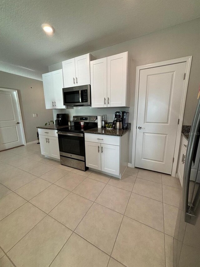 kitchen featuring white cabinetry, stainless steel appliances, light tile patterned flooring, and a textured ceiling