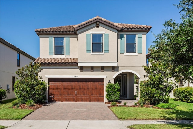 mediterranean / spanish home with stucco siding, a tiled roof, decorative driveway, and a garage