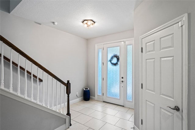 entrance foyer featuring stairs, light tile patterned floors, baseboards, and a textured ceiling