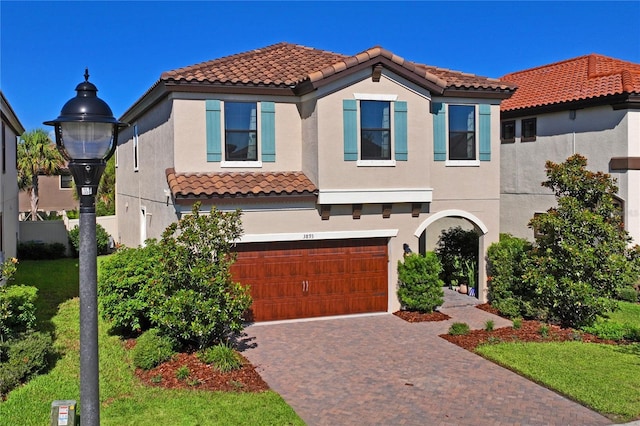 mediterranean / spanish house with a tile roof, decorative driveway, an attached garage, and stucco siding