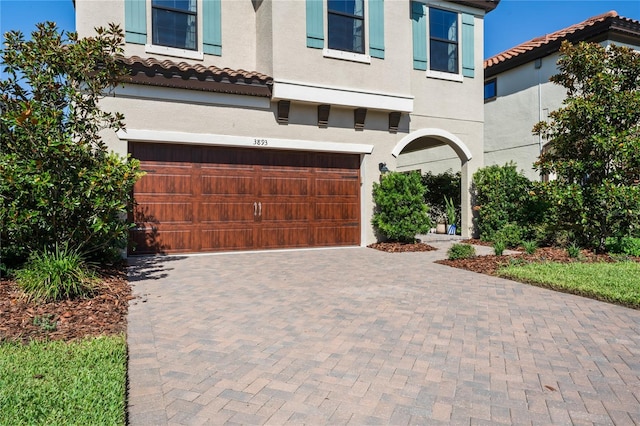 view of front of house featuring stucco siding, a tiled roof, decorative driveway, and a garage