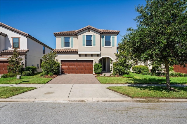 mediterranean / spanish house with a tile roof, a front yard, stucco siding, decorative driveway, and a garage