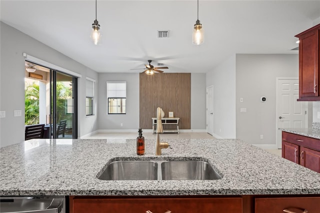 kitchen with a sink, open floor plan, reddish brown cabinets, ceiling fan, and light stone countertops