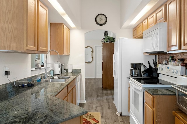 kitchen with white appliances, dark stone countertops, light wood-type flooring, light brown cabinetry, and sink