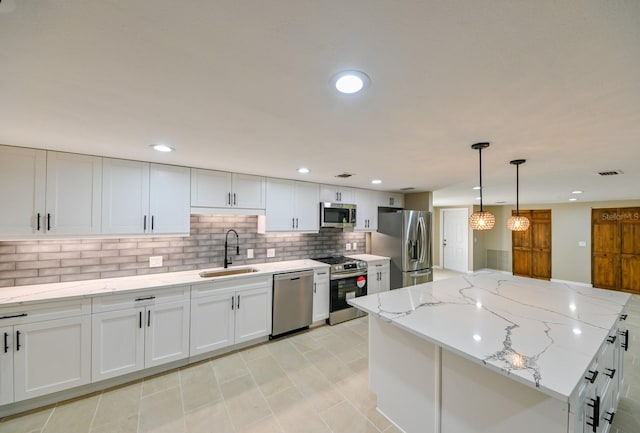 kitchen featuring sink, appliances with stainless steel finishes, a center island, light stone countertops, and white cabinets