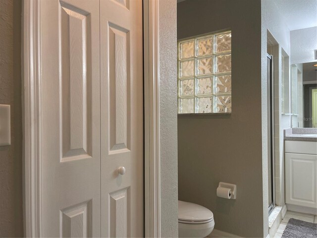 bathroom with tile patterned floors, vanity, toilet, a shower with shower door, and a textured ceiling