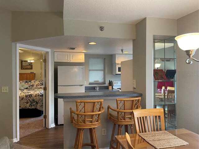 kitchen with a textured ceiling, a breakfast bar area, white appliances, dark hardwood / wood-style flooring, and white cabinetry