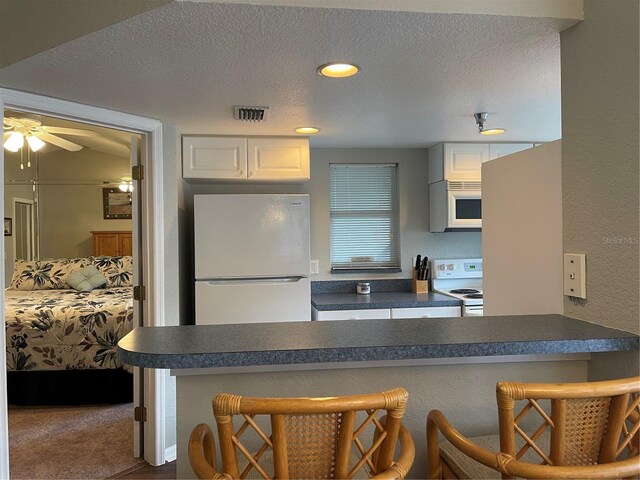 kitchen with white cabinets, a textured ceiling, white appliances, ceiling fan, and a breakfast bar