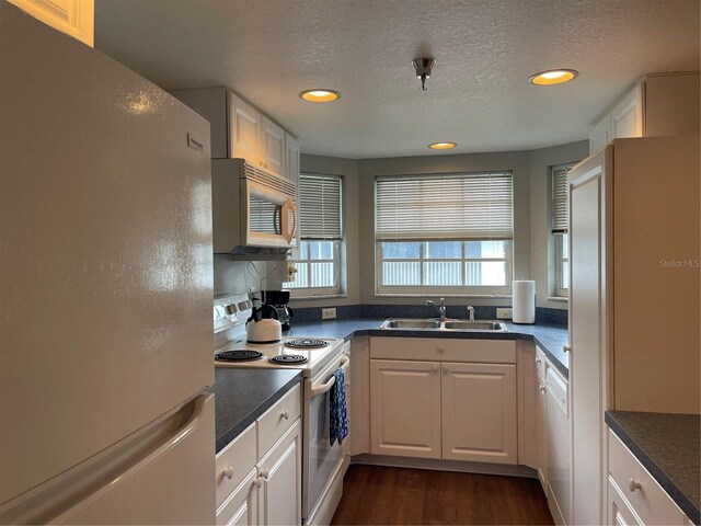 kitchen featuring a textured ceiling, white appliances, dark wood-type flooring, sink, and white cabinets