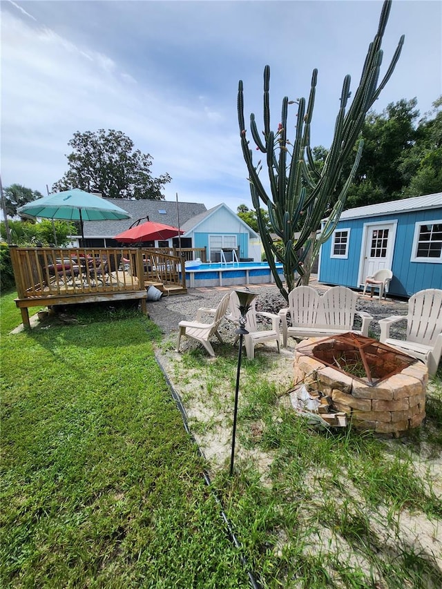 view of yard with an outdoor structure, a swimming pool side deck, and an outdoor fire pit