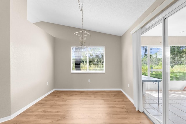 unfurnished dining area featuring a chandelier, a textured ceiling, light hardwood / wood-style flooring, and vaulted ceiling