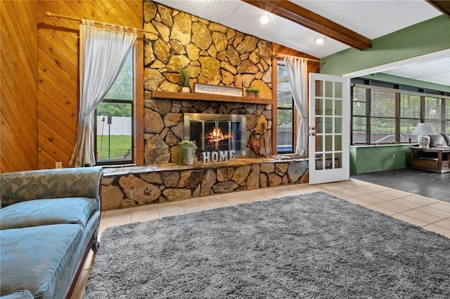 living room featuring a stone fireplace, wooden walls, beam ceiling, and tile patterned floors