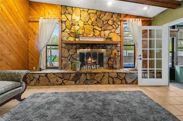 tiled living room featuring a textured ceiling, wood walls, a stone fireplace, french doors, and lofted ceiling