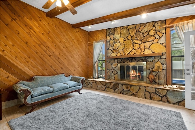 living room with wood walls, beamed ceiling, a fireplace, tile patterned floors, and ceiling fan