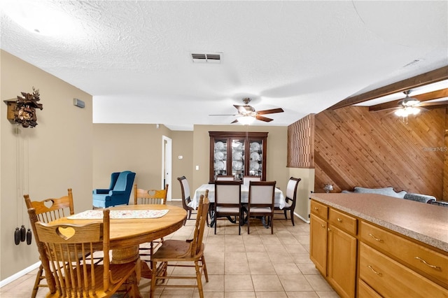 dining space featuring a textured ceiling, light tile patterned flooring, wood walls, and ceiling fan