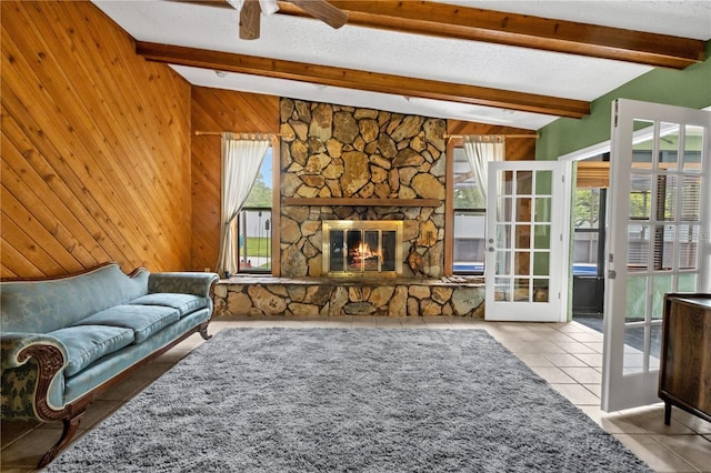 living room featuring ceiling fan, wood walls, a stone fireplace, and lofted ceiling with beams