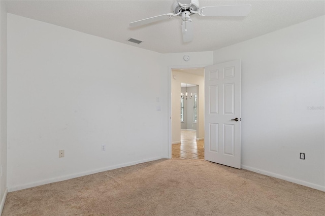 spare room featuring ceiling fan with notable chandelier and light colored carpet