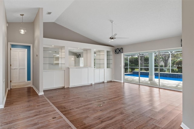 unfurnished living room featuring hardwood / wood-style floors, a textured ceiling, lofted ceiling, built in shelves, and ceiling fan