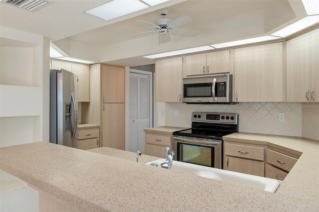 kitchen featuring ceiling fan, kitchen peninsula, sink, appliances with stainless steel finishes, and light brown cabinetry