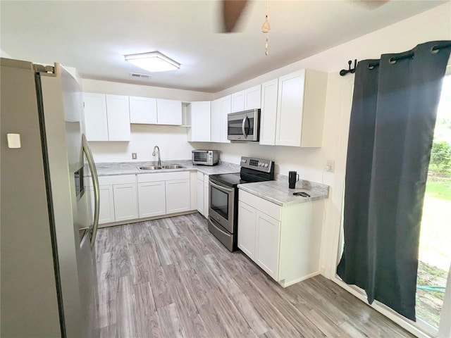 kitchen with sink, light wood-type flooring, white cabinetry, and appliances with stainless steel finishes