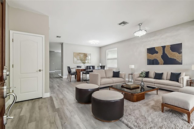 living room featuring light wood-style flooring, baseboards, and visible vents