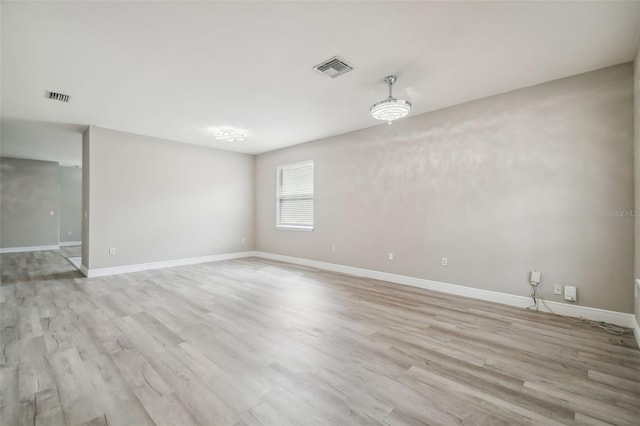 empty room featuring light wood finished floors, visible vents, and baseboards