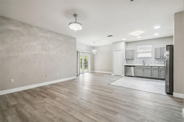 unfurnished living room featuring visible vents, light wood-type flooring, baseboards, and a sink