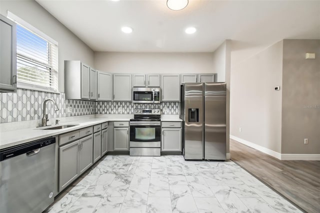 kitchen with gray cabinets, a sink, decorative backsplash, appliances with stainless steel finishes, and marble finish floor