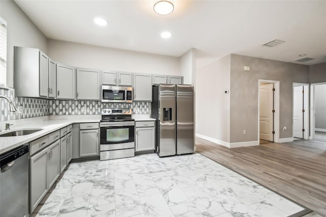 kitchen with a sink, gray cabinetry, light countertops, appliances with stainless steel finishes, and backsplash