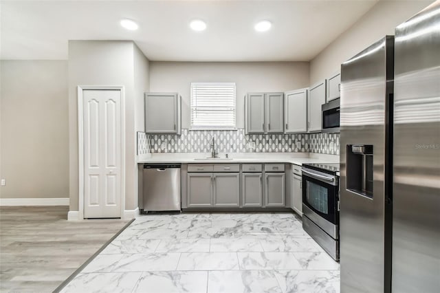 kitchen featuring gray cabinets, a sink, light countertops, appliances with stainless steel finishes, and tasteful backsplash