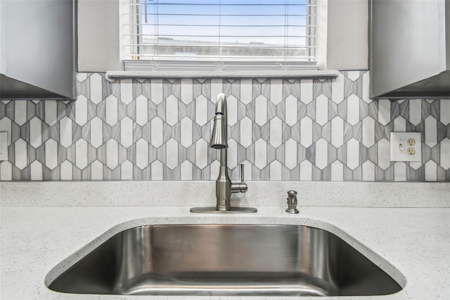 details featuring tasteful backsplash, light stone countertops, and a sink