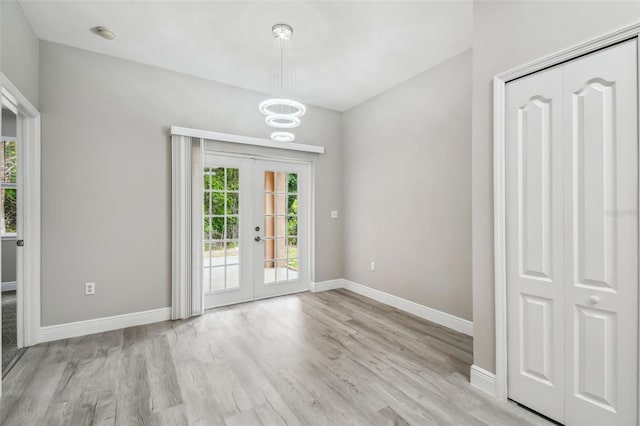 interior space with a notable chandelier, french doors, light wood-type flooring, and baseboards