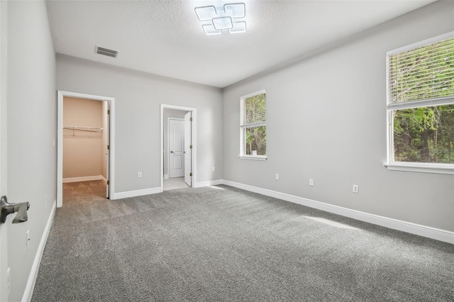 unfurnished bedroom with carpet, visible vents, baseboards, a spacious closet, and a textured ceiling