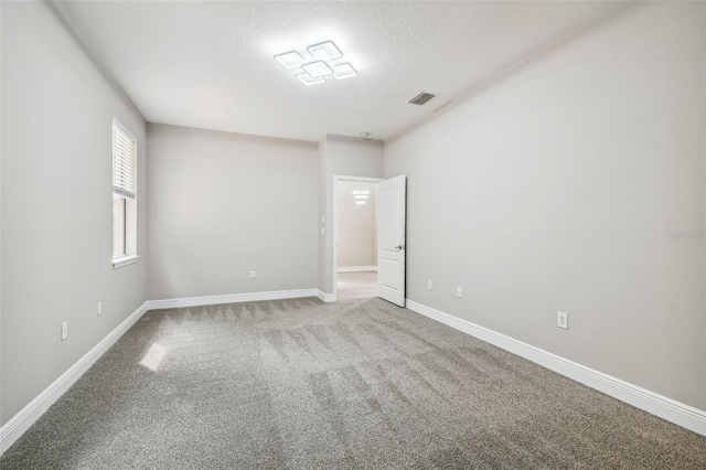 spare room featuring visible vents, baseboards, carpet floors, and a textured ceiling