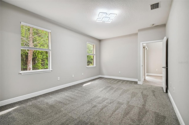 carpeted spare room featuring visible vents, a textured ceiling, and baseboards