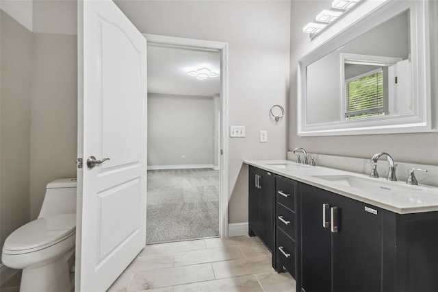 bathroom featuring double vanity, toilet, baseboards, and a sink