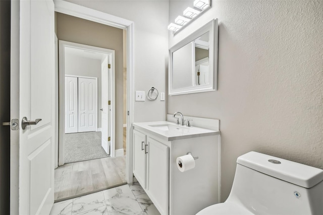 half bath featuring marble finish floor, toilet, and vanity