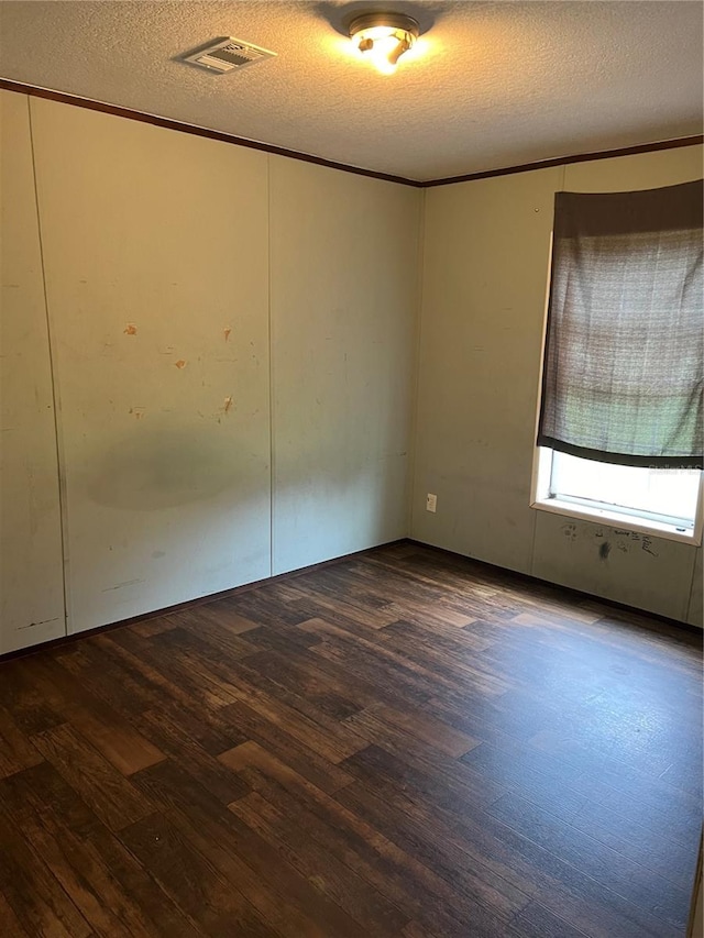 empty room featuring a textured ceiling, crown molding, and dark hardwood / wood-style flooring